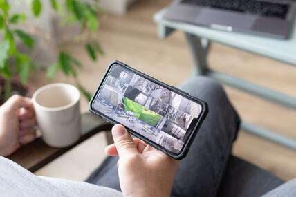 Person mit Smartphone in der Hand mit mehreren Kameraansichten von Bürostandorten