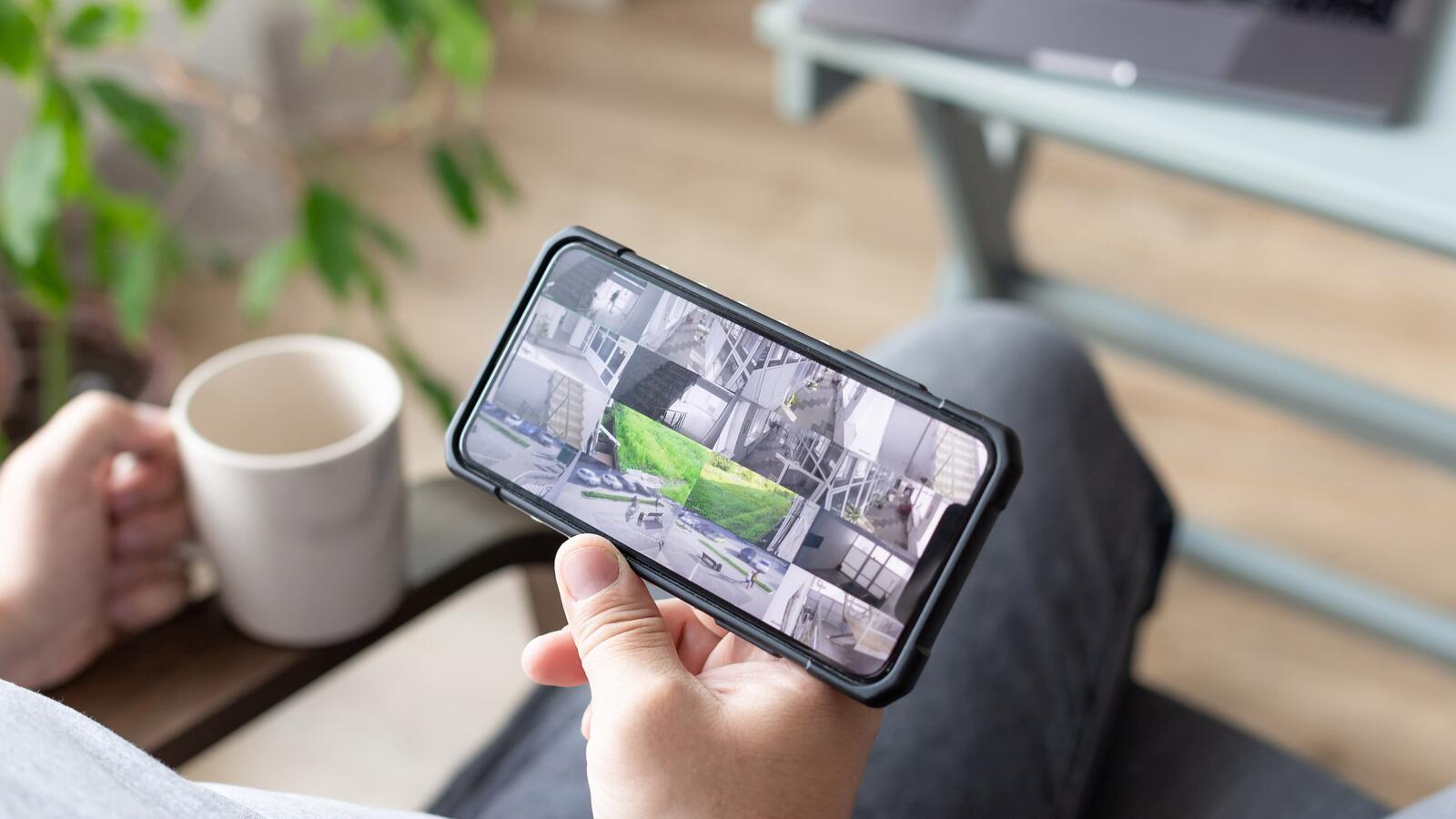 Person mit Smartphone in der Hand mit mehreren Kameraansichten von Bürostandorten